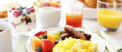 A breakfast plate with scrambled eggs, sausages, strawberries, blueberries, and a glass of orange juice.