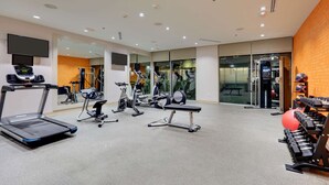 A modern gym with various exercise equipment, a mirrored wall, and a television screen. - La Quinta Inn & Suites by Wyndham Lakeway (Lakeway)