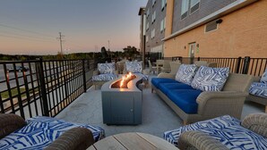 An outdoor seating area with wicker furniture, a fire pit, and a view of a building in the background. - La Quinta Inn & Suites by Wyndham Lakeway (Lakeway)