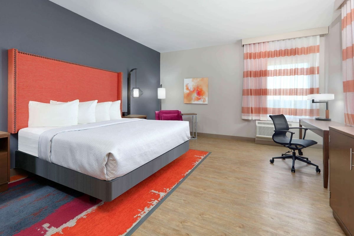 A hotel room with a bed, desk, chair, and a window with curtains.