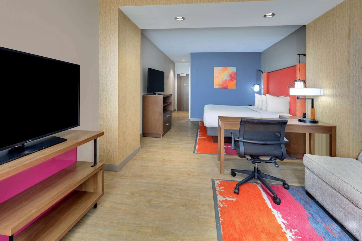 A hotel room with a flat-screen TV, a desk with a chair, a bed, and a sofa.