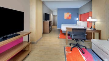 A hotel room with a flat-screen TV, a desk with a chair, a bed, and a sofa.