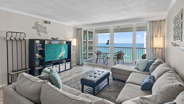 A modern living room with a flat-screen TV, a sofa, and a balcony with a view of the sea.