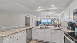 A modern kitchen with white cabinetry, a marble countertop, and a view to the outside.