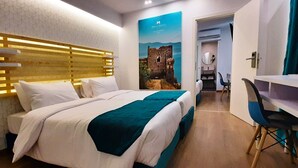 A hotel room with a large bed, a desk, and a chair. There is a poster on the wall and a door leading to another room. - Athenian Montaza Hotel (Kallithea)