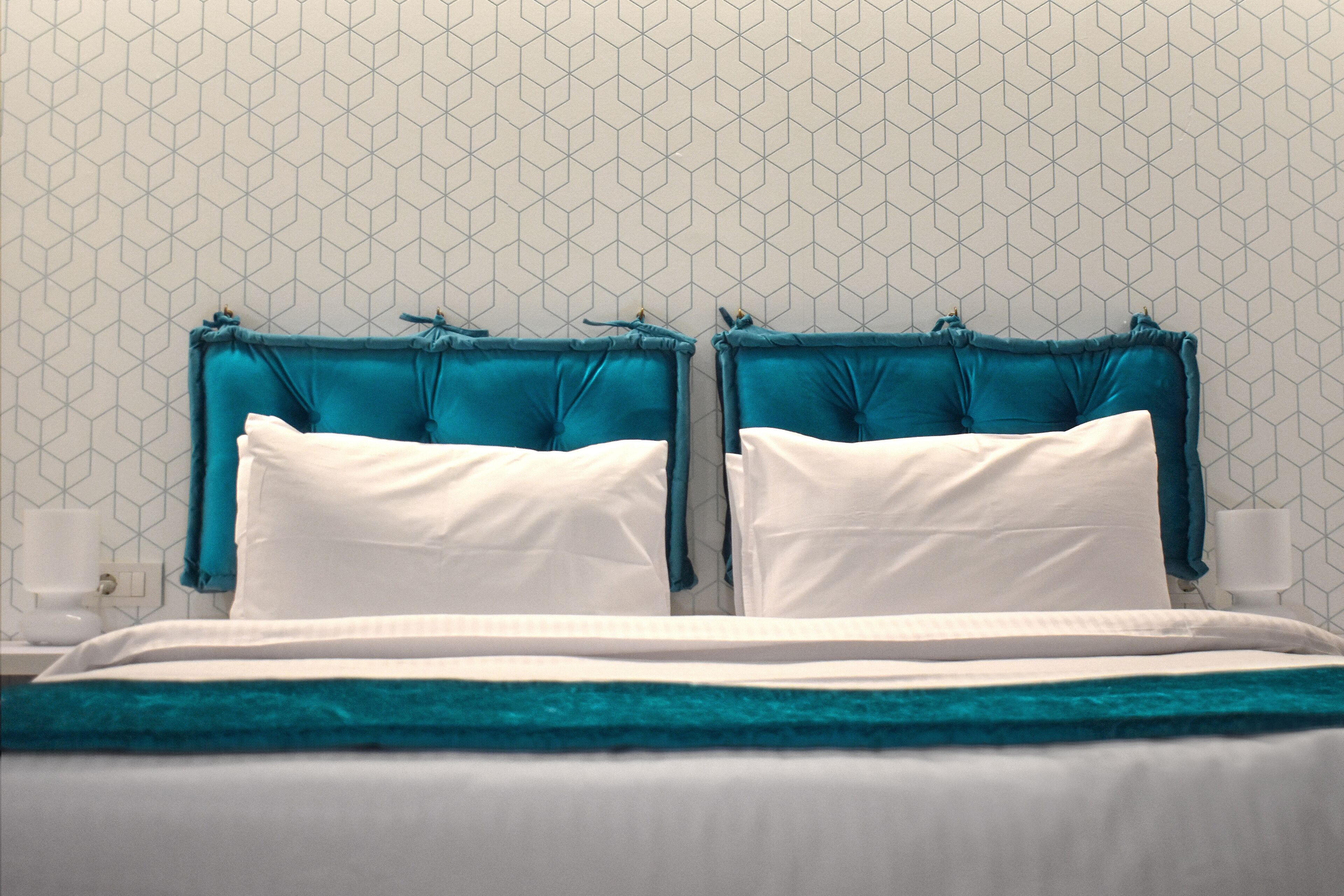 Un lit bien fait, avec une literie blanche et turquoise, une tête de lit turquoise et un mur orné d’un motif géométrique.