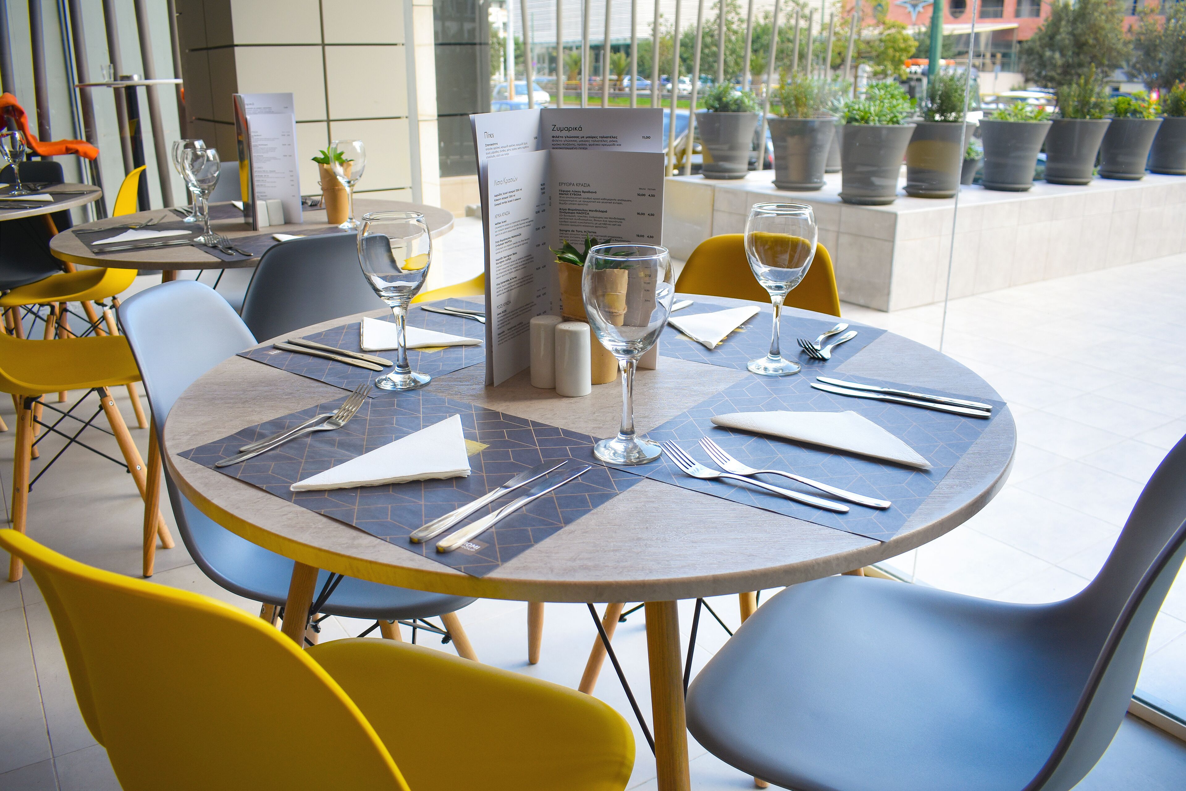 Une table de restaurant dressée avec un menu, des verres à vin et des couverts.