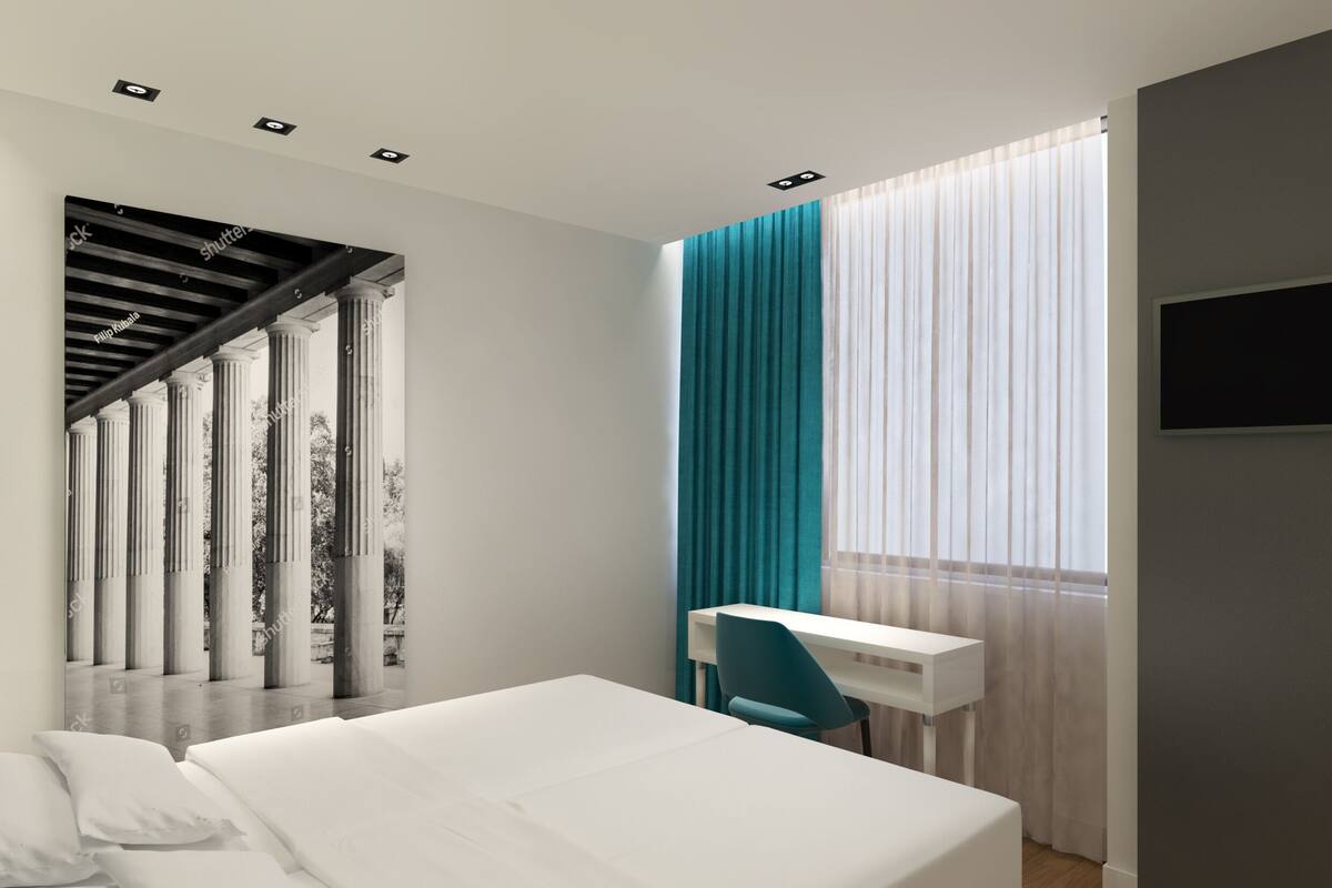 Moderni hotellihuone, jossa on sänky, työpöytä ja tuoli. Huoneessa on portaikko pylväineen, ja ikkunasta avautuu näkymä puita kohti.