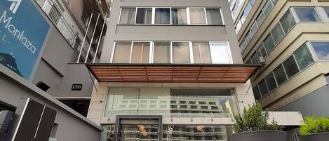 A modern hotel entrance with a glass facade, outdoor seating, and a sign for 'Montaza Hotel'.