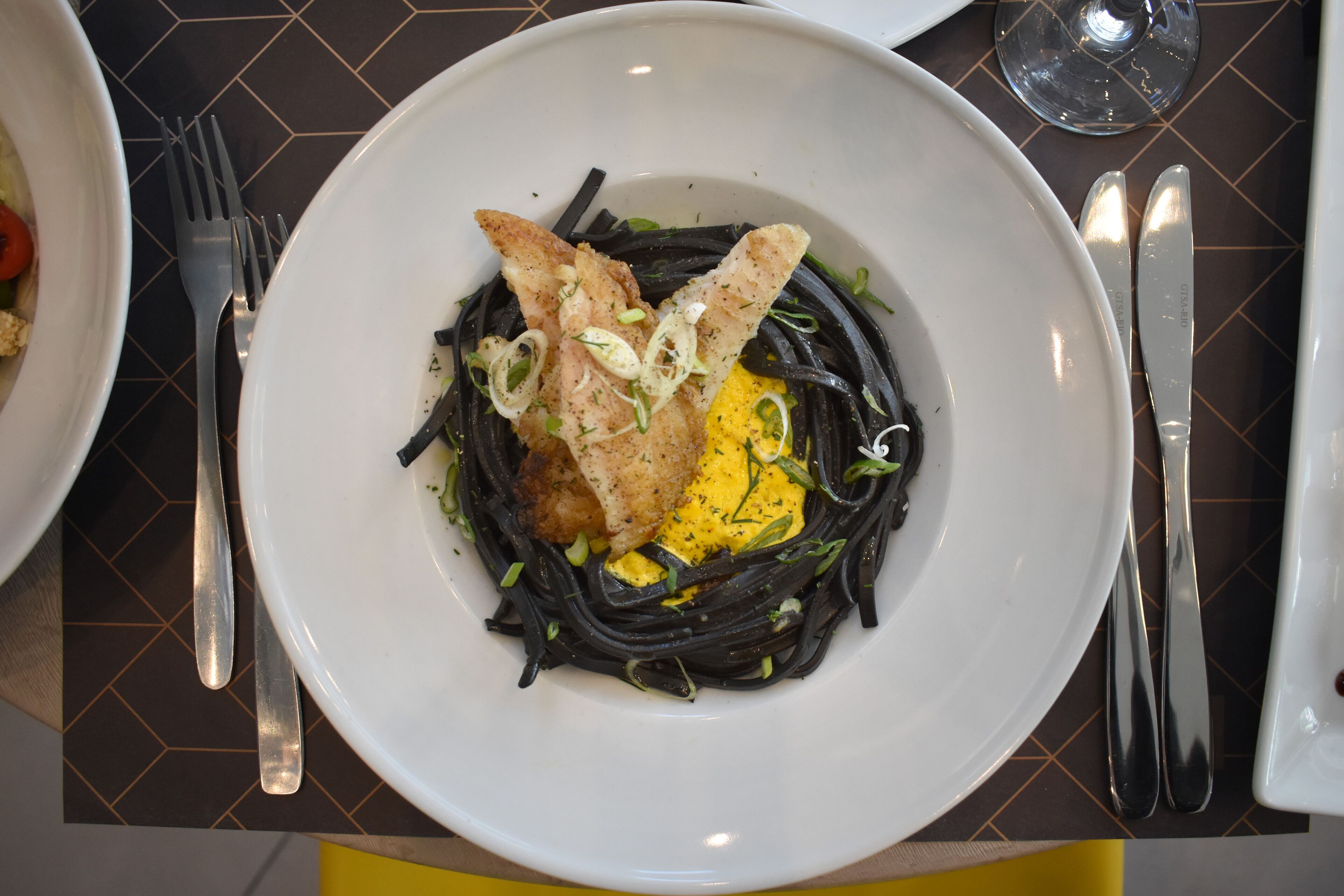 Une assiette de nouilles noires, accompagnée d’un morceau de poulet frit et d’un œuf jaune placé sur le dessus, le tout servi dans une assiette blanche.