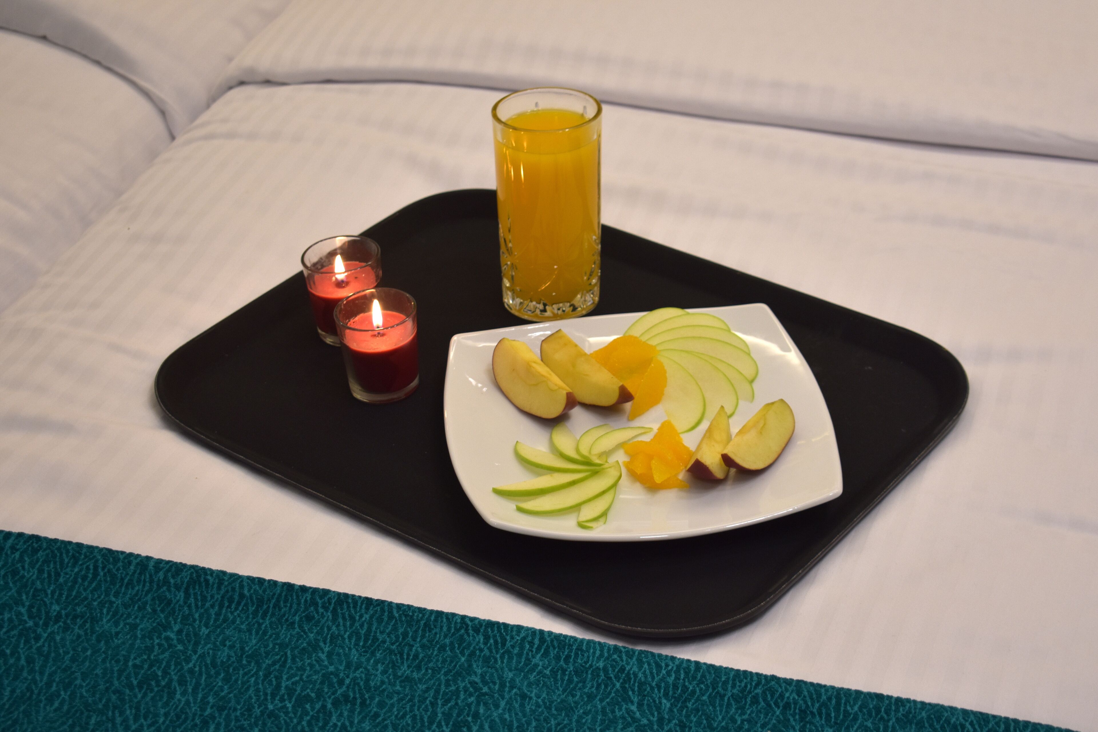 Bandeja con una fuente de frutas en rodajas y un vaso de jugo de naranja sobre una cama.