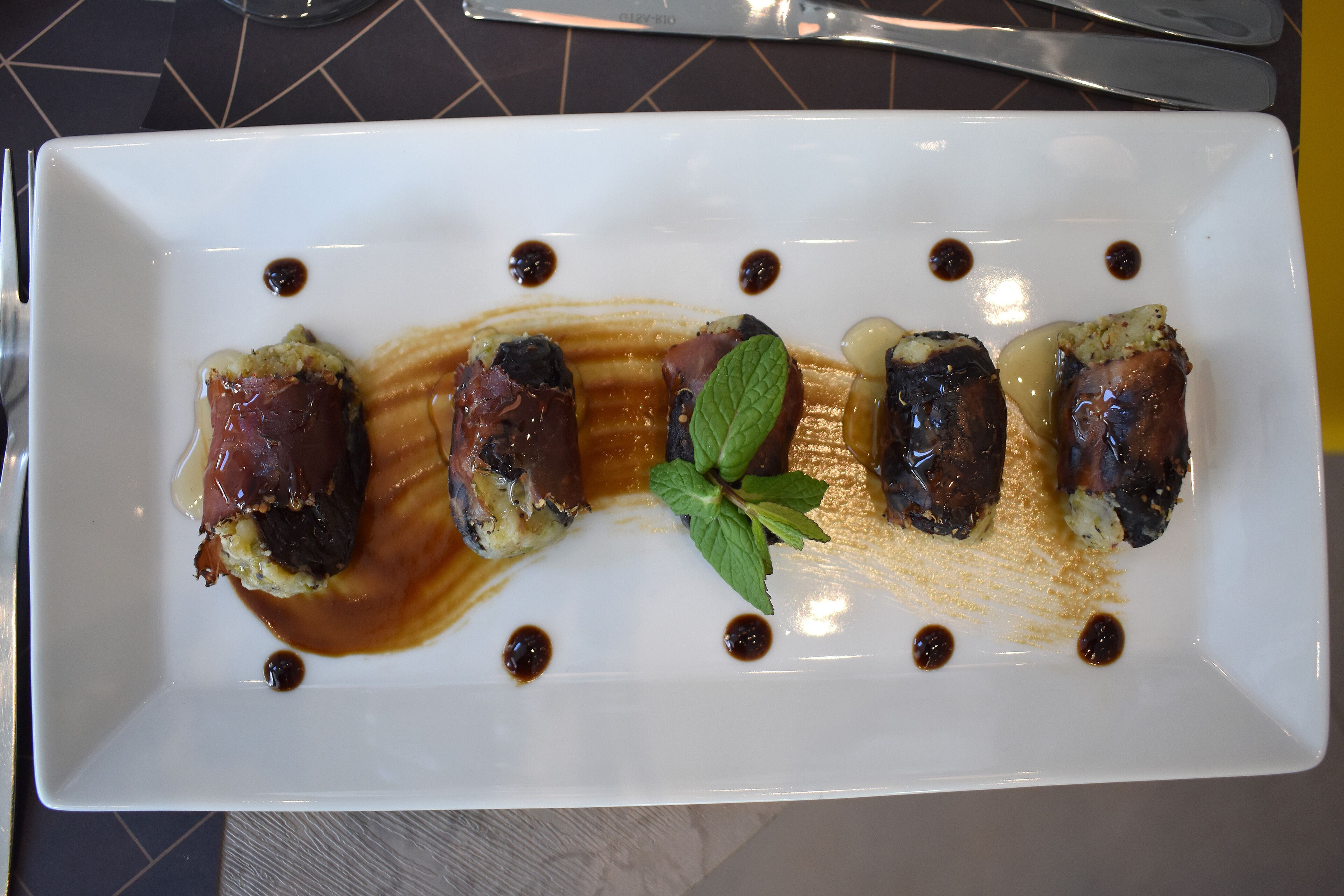 A rectangular white plate with four pieces of food, each with a sauce and a mint leaf garnish.