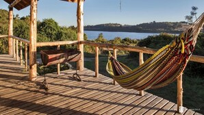 A wooden deck with a hammock and a grill, overlooking a lake and forest. - Antuquelen Lodge Cabañas (Frutillar)