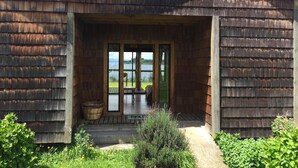 A wooden cabin with a large glass door leading to a deck, surrounded by greenery. - Antuquelen Lodge Cabañas (Frutillar)