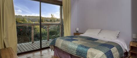 A bedroom with a large window, wooden floor, and a bed with a quilt.