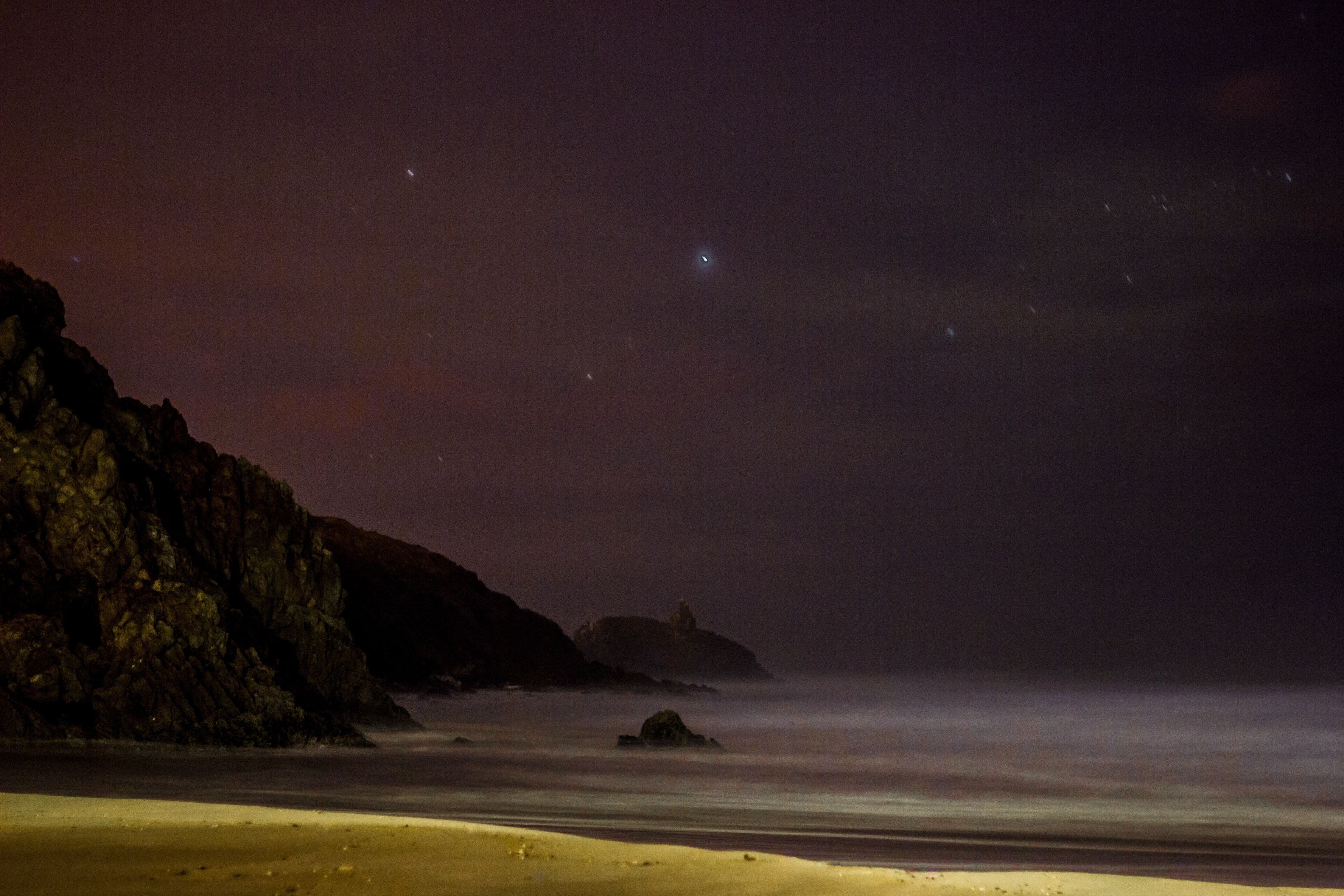Une plage de nuit, avec un rivage rocheux et une vue dégagée sur l’océan.