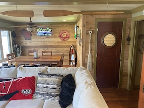 Relax in this inviting room with a sofa, dining table, and wooden wall featuring a unique neon sign and plaque.