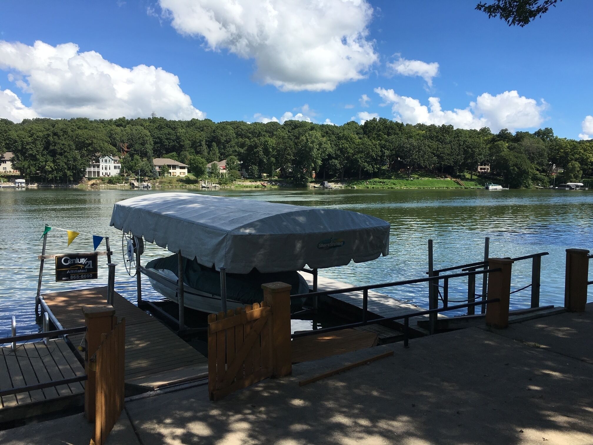 A dock with a covered boat, a wooden walkway, and a view of a lake with houses in the background.
