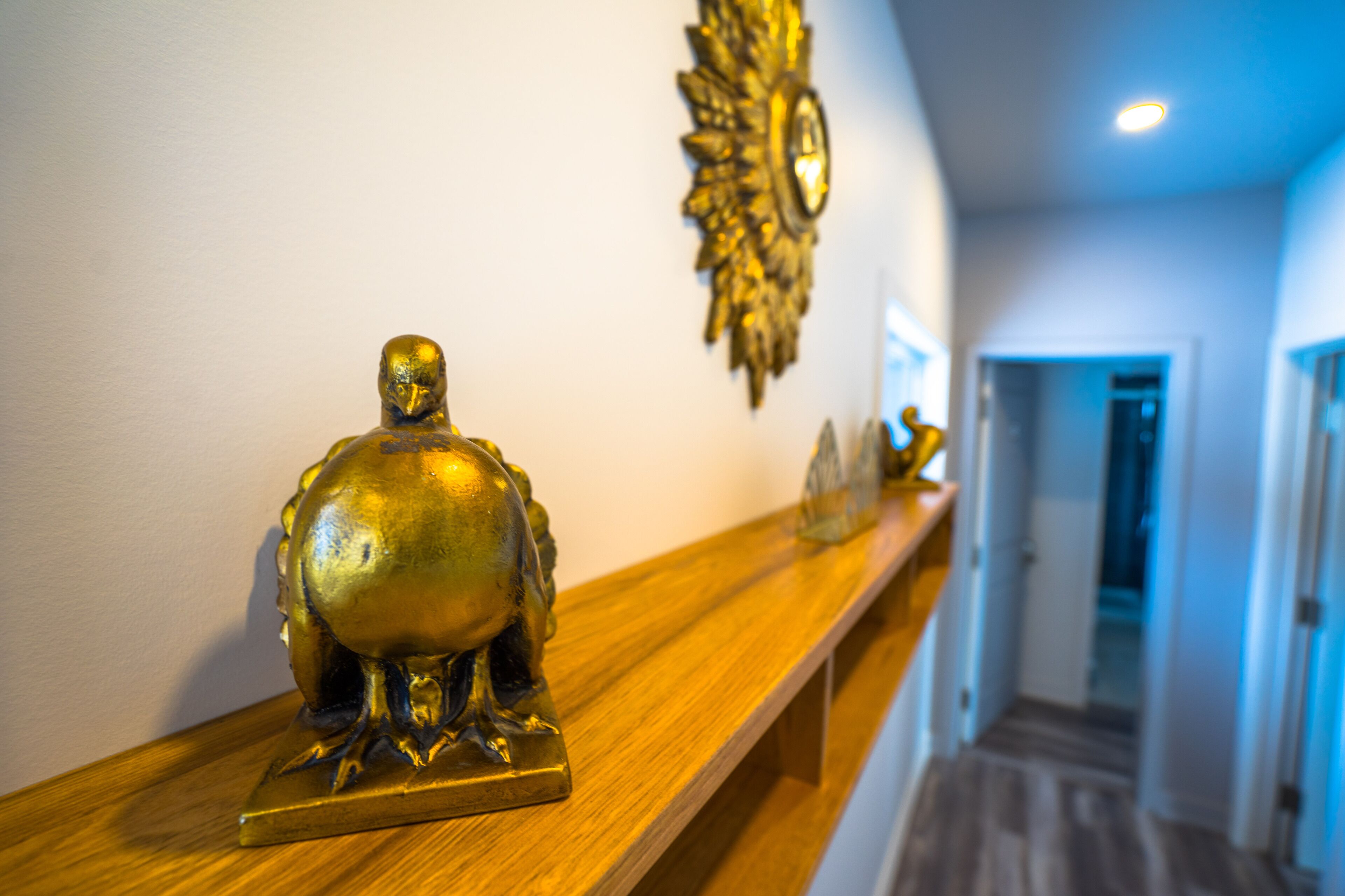 Un pasillo con un estante de madera que exhibe una estatua dorada, un adorno de pared y una puerta que da a otra habitación.