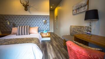 Una habitación de hotel con un cabecero capitonado, una cama con ropa de cama a rayas, una mesita de noche de madera, un escritorio con una lámpara y una manta roja.