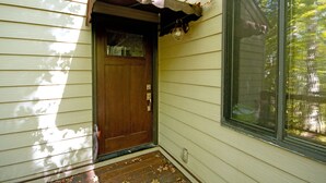 A wooden front door with a glass panel, a window to the right, and a small porch area with a decorative awning.