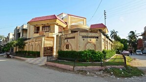 A two-story building with a red-tiled roof, a gated entrance, and a small garden area. - BlueSky Guest House (Karachi)