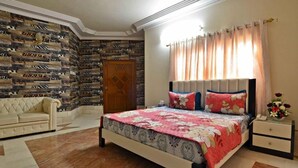 A bedroom with a bed, a nightstand, a dresser, a sofa, and a patterned wall. - BlueSky Guest House (Karachi)