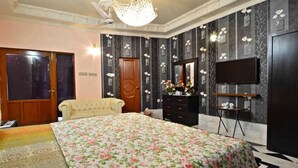 A bedroom with a floral bedspread, a chandelier, a television, and a dresser. - BlueSky Guest House (Karachi)