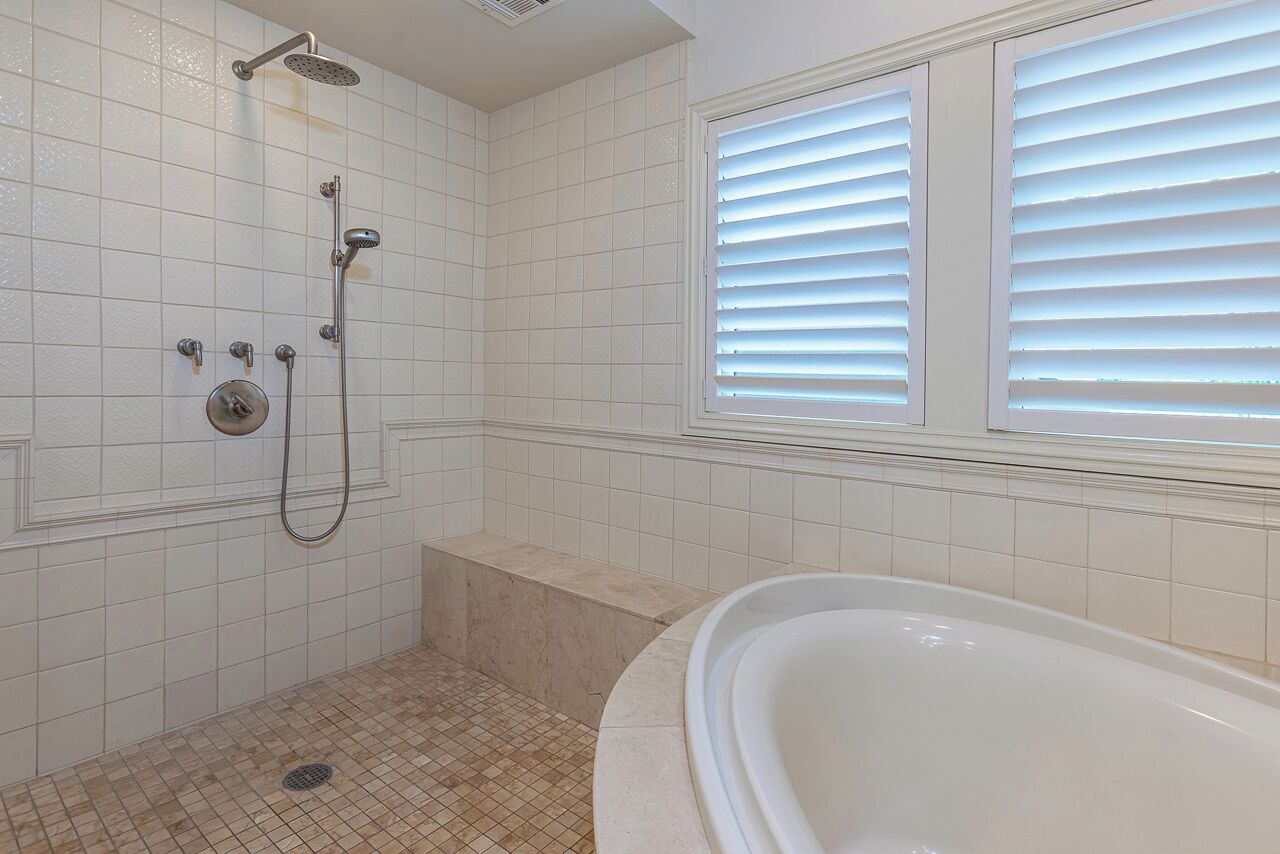 Une salle de bain avec une douche à l’italienne, une baignoire et une fenêtre équipée de stores.