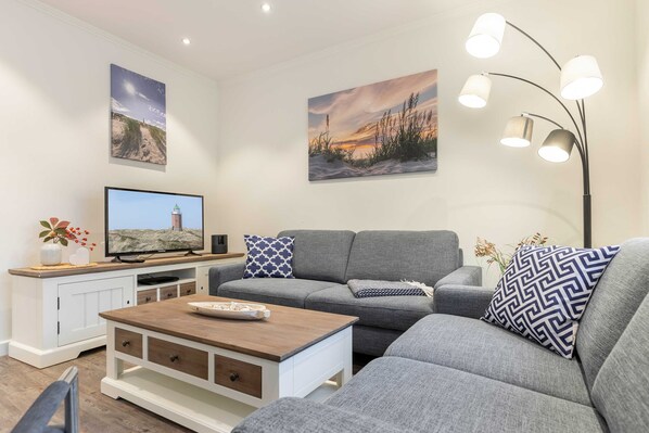 Un soggiorno moderno con un divano grigio, un tavolino in legno, una TV a schermo piatto e opere d'arte alle pareti.