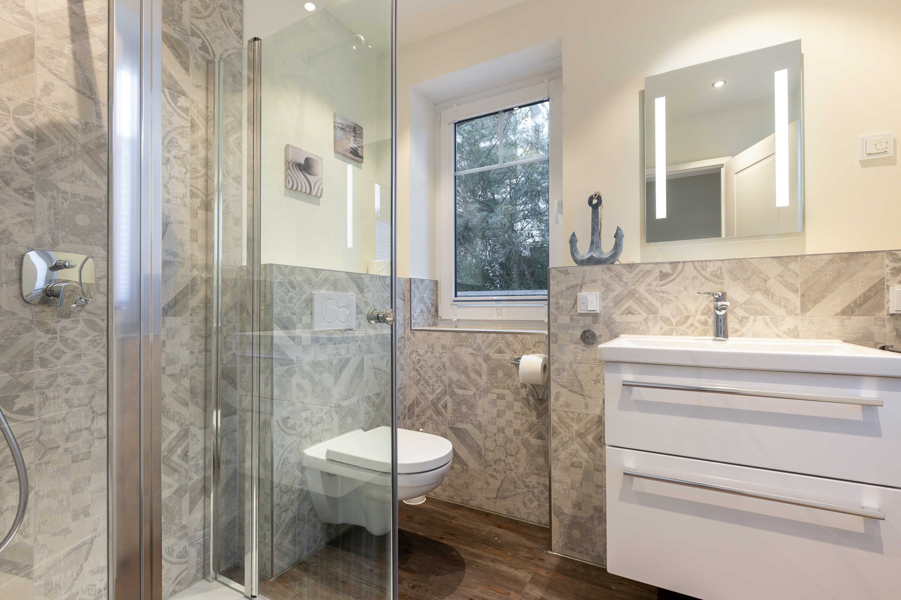 Un bany modern amb plat de dutxa de vidre, vàter i un lavabo amb mirall.