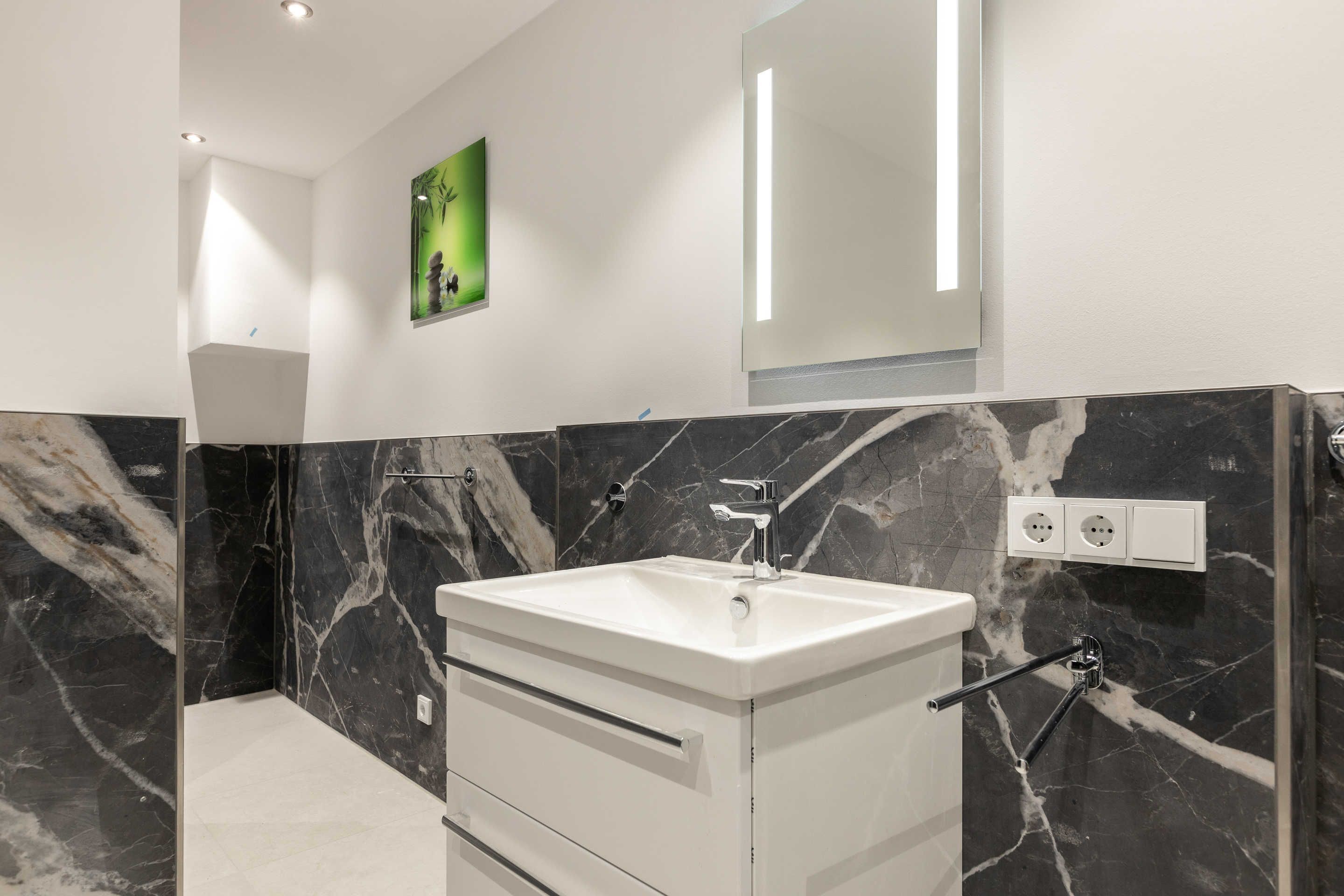 A modern bathroom with a white vanity, marble walls, and a large mirror.