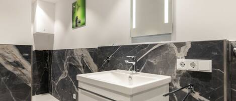 A modern bathroom with a white vanity, marble walls, and a large mirror.