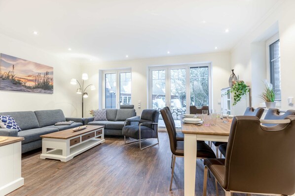A modern living room with a grey sofa, a wooden coffee table, and a dining area with a wooden table and chairs.