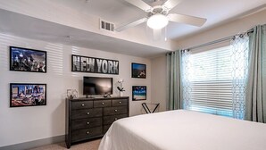 A bedroom with a bed, dresser, ceiling fan, and wall art.