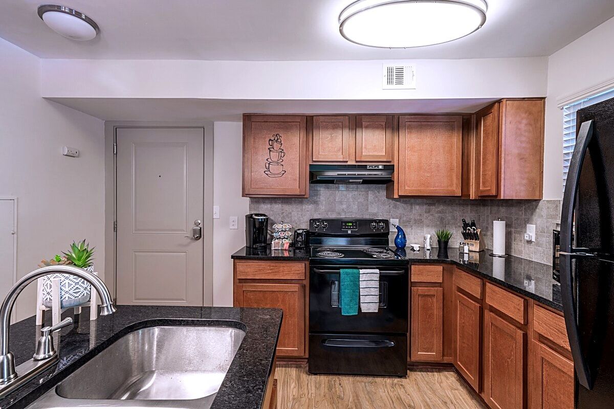 A modern kitchen with wooden cabinets, a stainless steel sink, a black stove, and a black refrigerator.