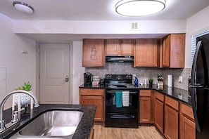 A modern kitchen with wooden cabinets, a stainless steel sink, a black stove, and a black refrigerator. - Walk to Aquarium & Stadiums · Free Parking (Atlanta)