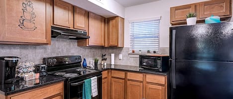 A kitchen with wooden cabinets, a black refrigerator, a stove, and a microwave.