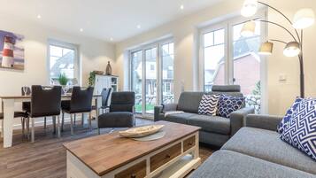 A modern living room with a dining area, large windows, and a view of the outside.