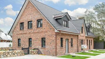 A two-story brick house with a sloped roof, a stone wall, and a small front yard.