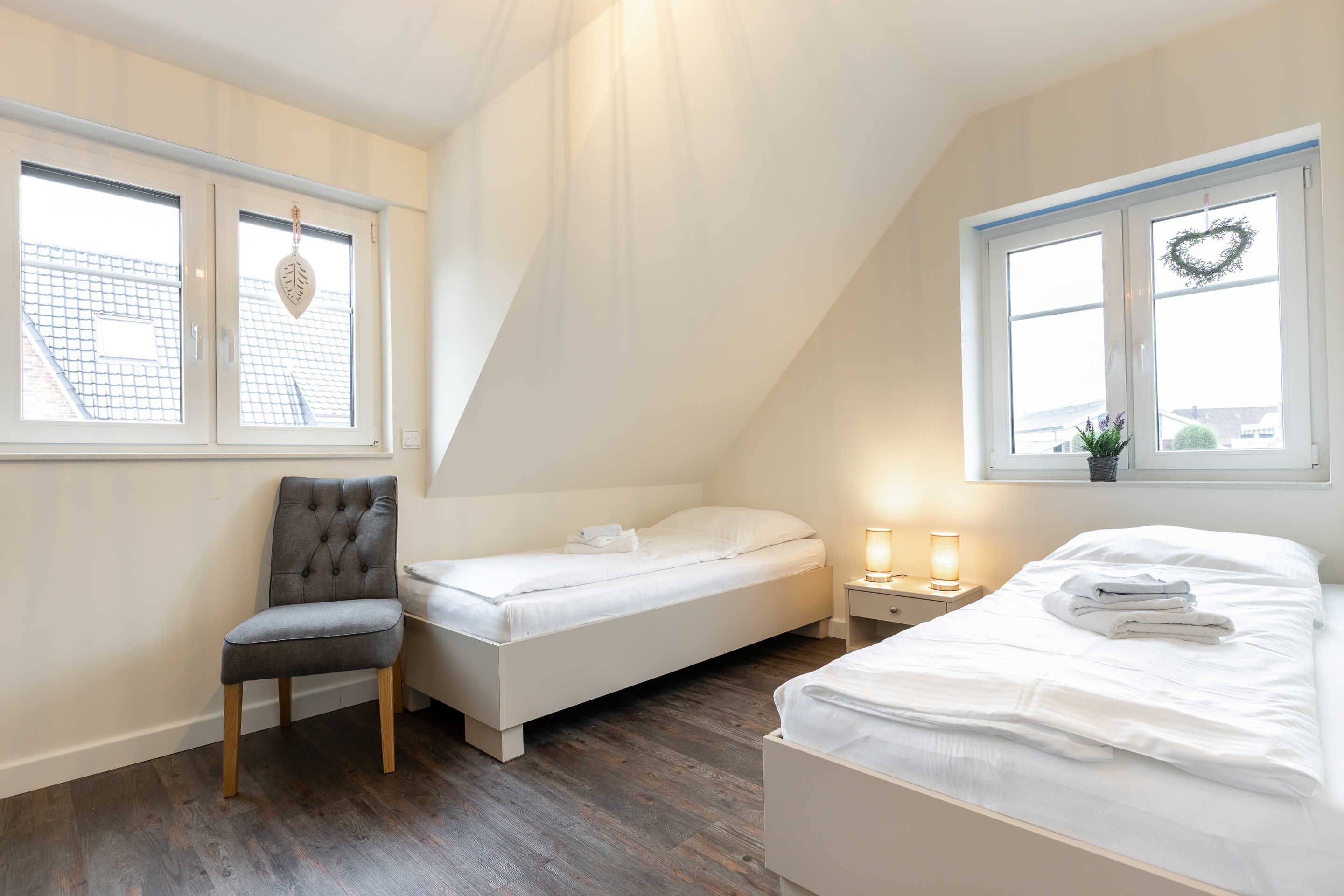 A bedroom with a loft bed, a single bed, a chair, and two bedside tables with lamps.
