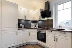 A modern kitchen with white cabinets, a black range hood, and a window providing natural light. - House Jensen 1, Germany (List)