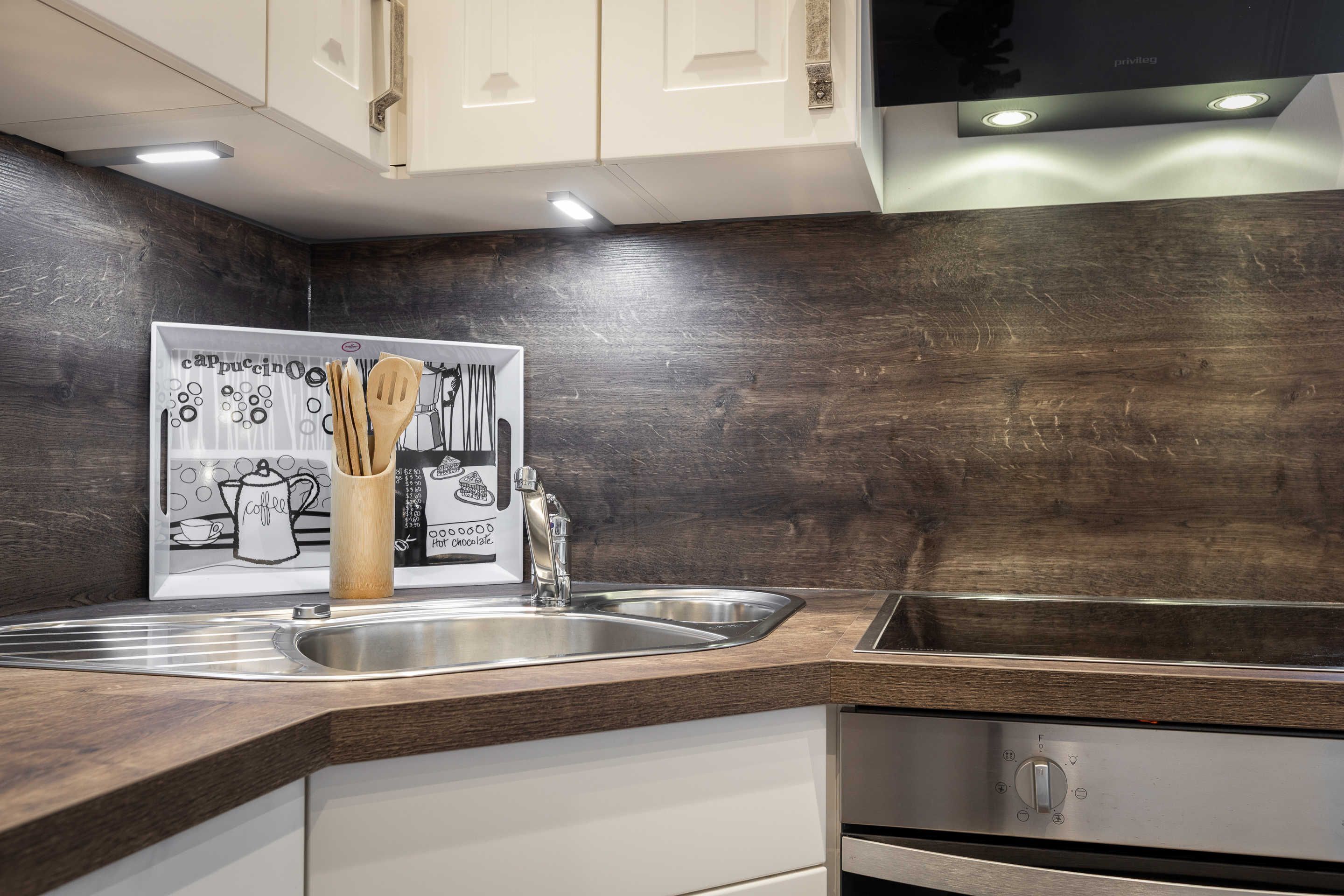 A modern kitchen with dark wooden cabinetry, stainless steel appliances, and a coffee-themed wall art.