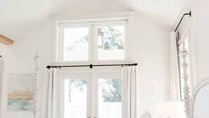 Ein Schlafzimmer mit einem Bett, einem Deckenventilator, einem Fenster mit Vorhängen und Blick ins Freie.