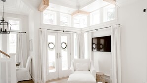 Ein heller, weißer Raum mit großem Fenster, einem weißen Sofa, einem kleinen Tisch und einem Deckenventilator.