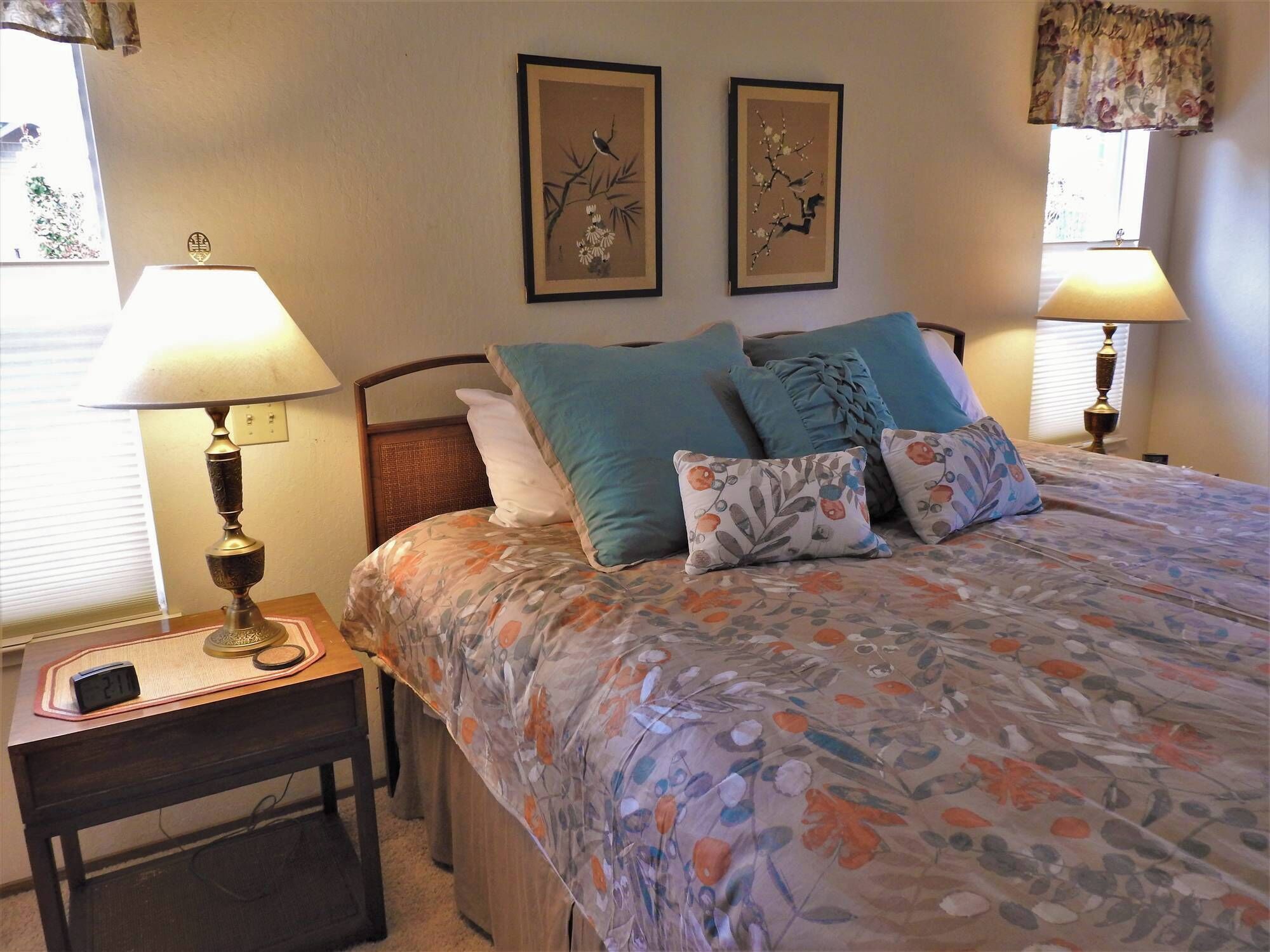 Quarto com uma cama, duas luminárias na parede, uma mesa de cabeceira com relógio e duas obras de arte emolduradas na parede.