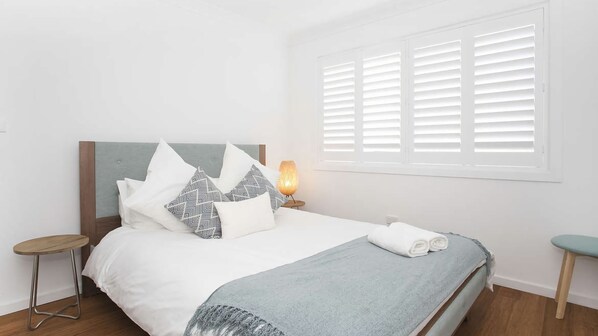 A neatly made bed with white and patterned pillows, a grey throw blanket, and a bedside lamp.