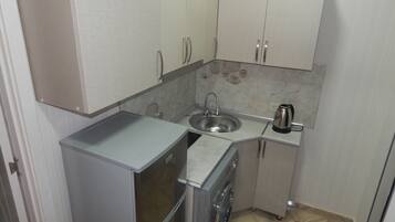 Een koelkast, een kookplaat, een waterkoker, kookgerei, borden en bestek