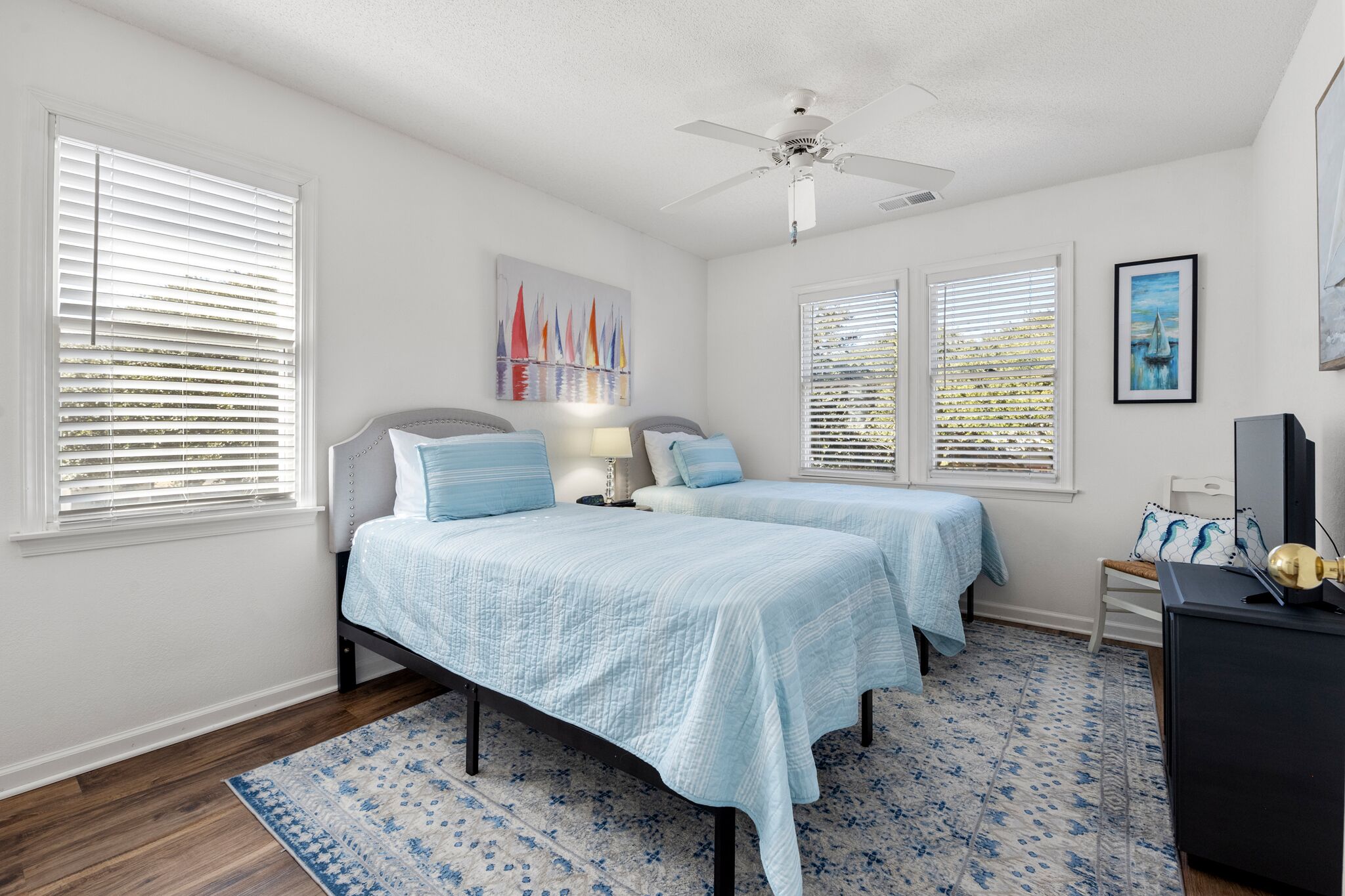 A bedroom with two beds, a ceiling fan, and artwork on the walls.