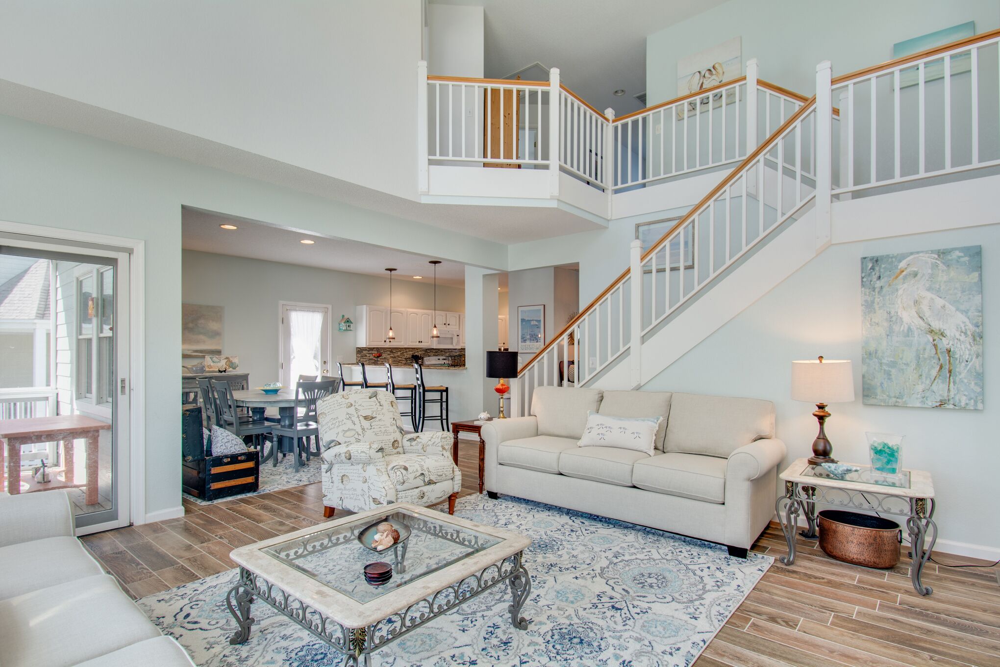 A spacious living room with a high ceiling, a staircase, and a dining area.